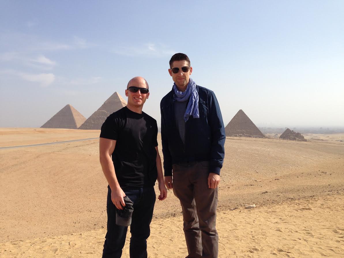 Two men standing with pyramids in background